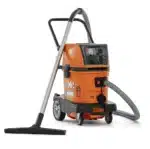 Husqvarna DE 35 H pölynimuri - oranssi teollisuus- ja rakennuspölynimuri letkulla, imukärjellä ja pyörillä.