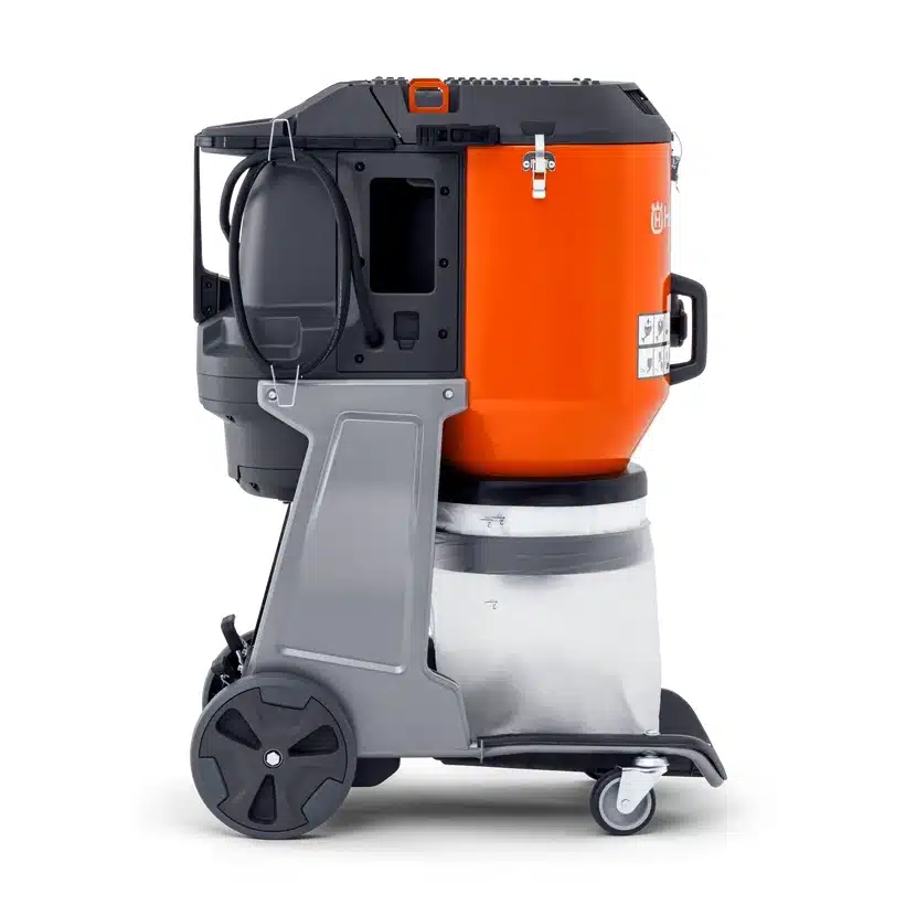 Husqvarna DE 120 SH -pölynerotinimuri sivusta kuvattuna, oranssi lieriömäinen runko harmaalla teräsrungolla, metallinen pölynkeräyssäiliö alhaalla, kaksi suurta takapyörää ja kaksi pientä kääntyvää etupyörää, virtajohto näkyvissä sivupaneelissa.