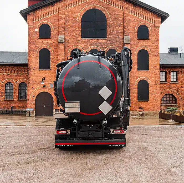 Musta SuperCombi-imupaineauto takaa kuvattuna tiilirakennuksen edessä, säiliön päädyssä punareunainen pyöreä kansi ja sivulla nostopuomi.