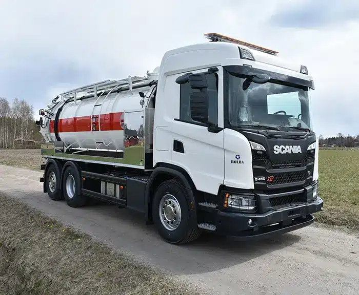 Valkoinen Scania-alustainen imupaineauto peltotien varrella, säiliössä punainen raitakoriste ja etuosassa pitkä imuputkisto.